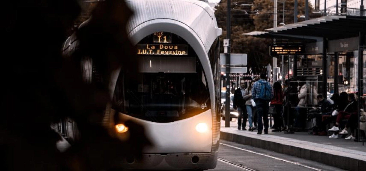 En premier plan, nous pouvons observer l'apparition du tram T1 arrivant à quai, en 2ème plan, nous pouvons voir les usagers attendant leur tram. 