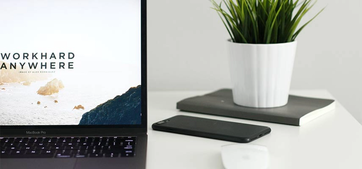 Au premier plan, à gauche, un MacBook Pro, ouvert, posé sur un bureau blanc, avec affiché sur son écran les mots 