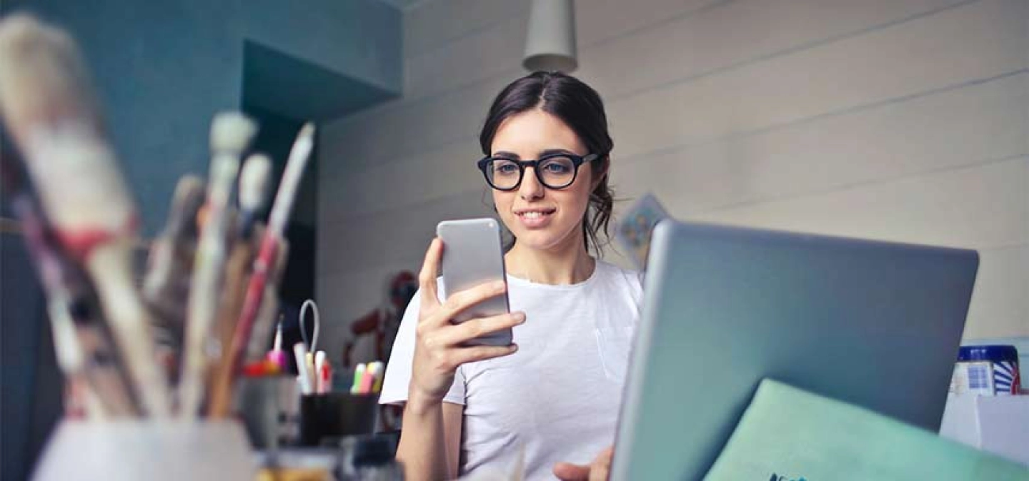 femme tenant son mobile devant un écran dans son atelier